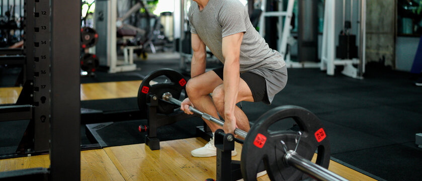 muscular body builder sport man is practice weight training on squat barbell for core muscle inside gym with dark background for exercising and workout usage