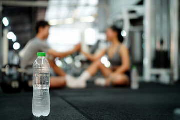 Asian woman and man sit in fitness gym with relax activity also look happiness after training and practice in fitness gym, focus water bottle on floor
