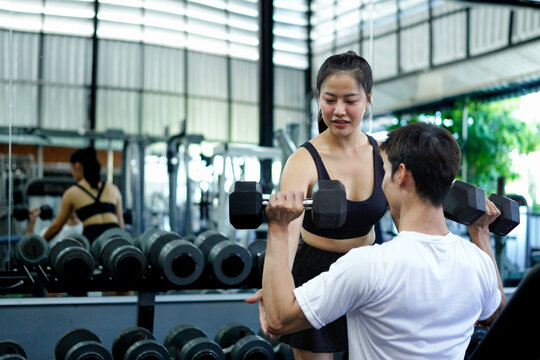 young sport man exercise lifting dumbbells on the bench in fitness gym healthy .Muscular man in sportswear training biceps with personal trainer woman workout.bodybuilding