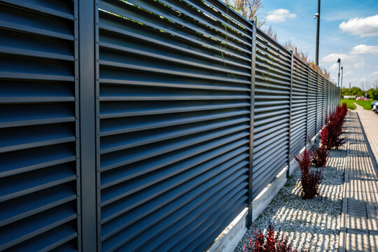 Modern Metal Louver Fence with Decorative Gravel and Red Shrubs in Industrial Landscaping and Garden Design Area