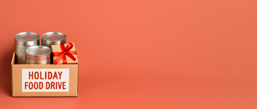 Holiday food drive box with canned goods and gift against orange background