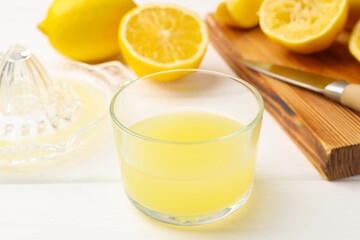 Lemon juice in glass, juicer and fresh lemons on white wooden table, closeup