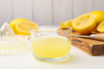 Lemon juice in glass, juicer and fresh lemons on white wooden table, closeup