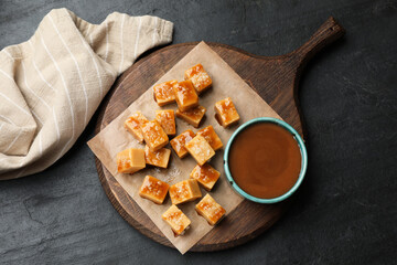 Tasty candies with salt and caramel sauce on dark textured table, top view