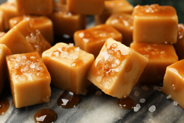 Tasty candies with salt and caramel sauce on dark marble table, closeup