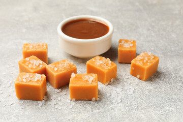 Tasty candies with salt and caramel sauce on grey textured table, closeup