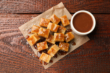 Tasty candies with salt and caramel sauce on wooden table, top view