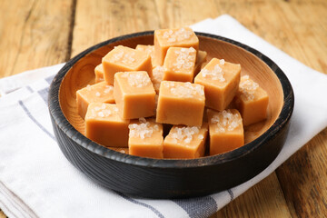 Tasty caramel candies with salt in bowl on wooden table, closeup