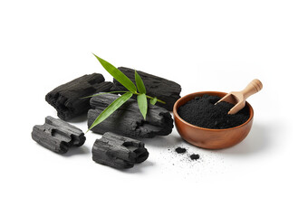 natural composition features several pieces of black charcoal chunks and a wooden bowl filled with fine black charcoal powder. A small wooden scoop holds more powder, and fresh green bamboo leaves add