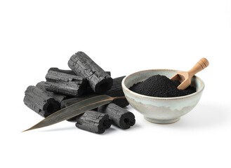 natural composition features several pieces of black charcoal chunks and a wooden bowl filled with fine black charcoal powder. A small wooden scoop holds more powder, and fresh green bamboo leaves add