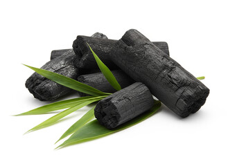 natural composition features several pieces of black charcoal chunks and a wooden bowl filled with fine black charcoal powder. A small wooden scoop holds more powder, and fresh green bamboo leaves add