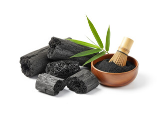 natural composition features several pieces of black charcoal chunks and a wooden bowl filled with fine black charcoal powder. A small wooden scoop holds more powder, and fresh green bamboo leaves add