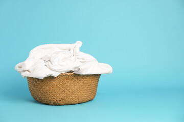 Wicker basket with laundry on light blue background, space for text