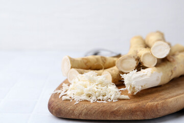 Fototapeta premium Grated horseradish and fresh roots on white tiled table, closeup. Space for text