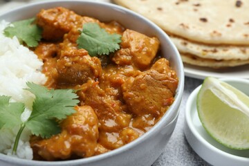 Delicious chicken tikka masala with rice, cilantro, lime and lavash on grey textured table, closeup