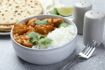 Delicious chicken tikka masala with rice, cilantro, spices and fork on grey textured table, closeup