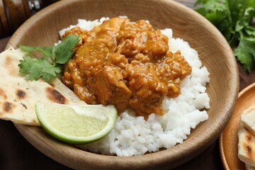 Delicious chicken tikka masala with rice, cilantro, lime and lavash in wooden bowl on table, closeup