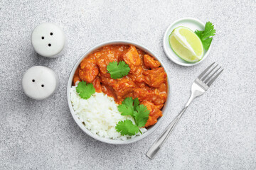 Delicious chicken tikka masala with rice, cilantro, lime and spices served on grey textured table, flat lay