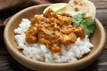 Delicious chicken tikka masala with rice, cilantro, lime and lavash in bowl on wooden table, closeup