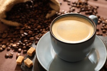 Aromatic coffee in cup, beans and brown sugar on table, closeup