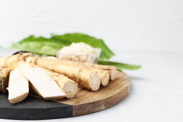 Whole and grated horseradish roots and green leaves on white table, closeup. Space for text
