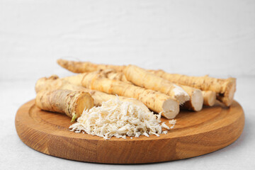 Whole and grated horseradish roots on light grey table, closeup