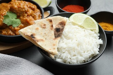 Delicious rice, lavash, lime, chicken tikka masala and spices on grey table, closeup