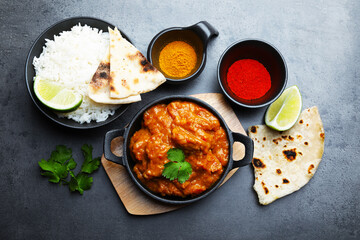 Delicious chicken tikka masala, rice, cilantro, lime, lavash and spices on grey textured table, flat lay