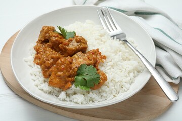 Delicious chicken tikka masala with rice, cilantro and fork on white wooden table, closeup