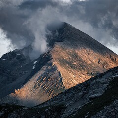 Dramatic Mountain Peak Bathed in Golden Hour Light with Stormy Clouds Above