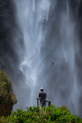 A man enjoying a hight waterfall cascading flow of water, surrounded by lush scenery. 