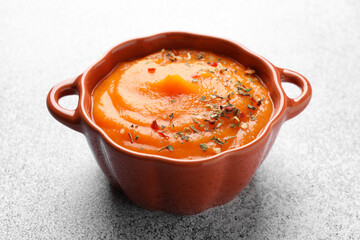 Tasty pumpkin cream soup served in pumpkin shaped bowl on grey table, closeup
