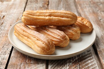 Tasty eclairs with powdered sugar on wooden table, closeup