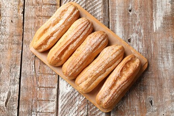 Tasty eclairs with powdered sugar on wooden table, top view