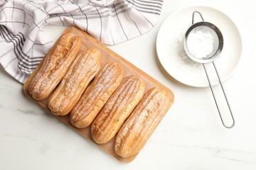 Tasty eclairs with powdered sugar on white marble table, top view