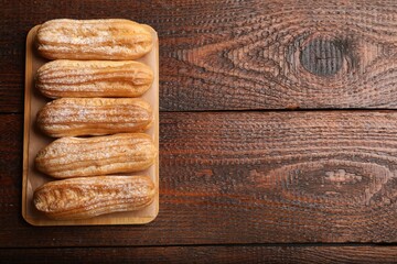 Tasty eclairs with powdered sugar on wooden table, top view. Space for text