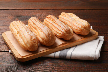 Tasty eclairs with powdered sugar on wooden table, closeup