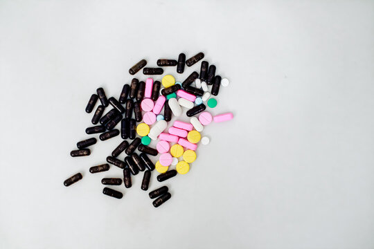Scattered mix of colorful pills and capsules on a white surface for healthcare