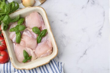 Raw chicken thighs with basil in baking dish and products on white marble table, flat lay. Space for text
