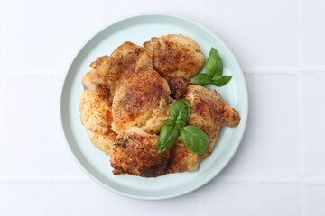 Tasty roasted chicken thighs with basil on white tiled table, top view
