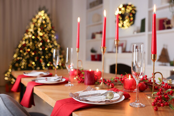 Stylish Christmas table setting with plates, glasses and burning candles in festive decorated room. Bokeh effect