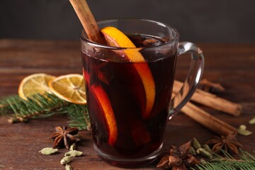 Tasty mulled wine in glass cup, spices and fir branches on wooden table against grey background, closeup