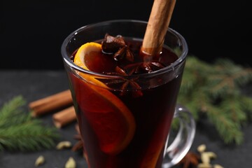Tasty mulled wine in glass mug, spices and fir branches on black table, closeup