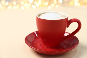Aromatic coffee in cup on beige background against Christmas lights, closeup. Space for text