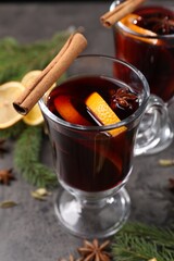 Tasty mulled wine in glass mugs, spices and fir branches on grey table, closeup