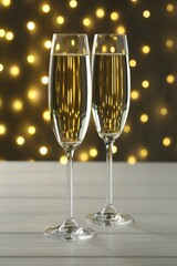 Merry Christmas and Happy New Year. Flute glasses with sparkling wine on white wooden table against dark background with blurred lights, closeup