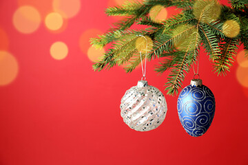 Christmas baubles hanging on fir tree branches against red background with blurred lights, closeup with space for text. Bokeh effect