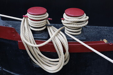 Red and black metal mooring bollards with ropes tied to anchor boat