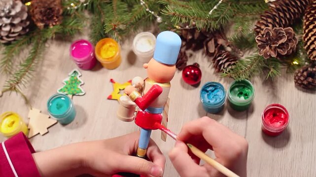 Children's hands paint wooden toy fairytale Nutcracker with spruce branches on table
