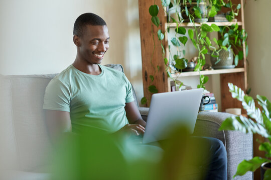 Smiling young African man using a laptop on his sofa